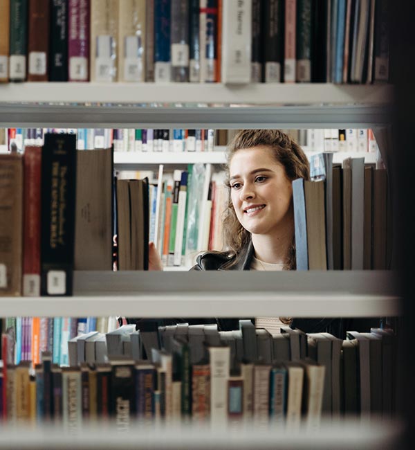Person browsing books on library shelves.