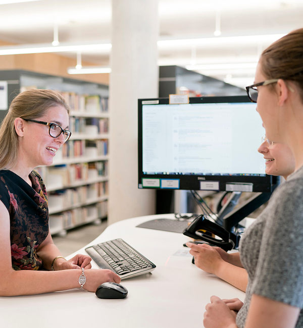 Library staff providing help at a computer in the library.