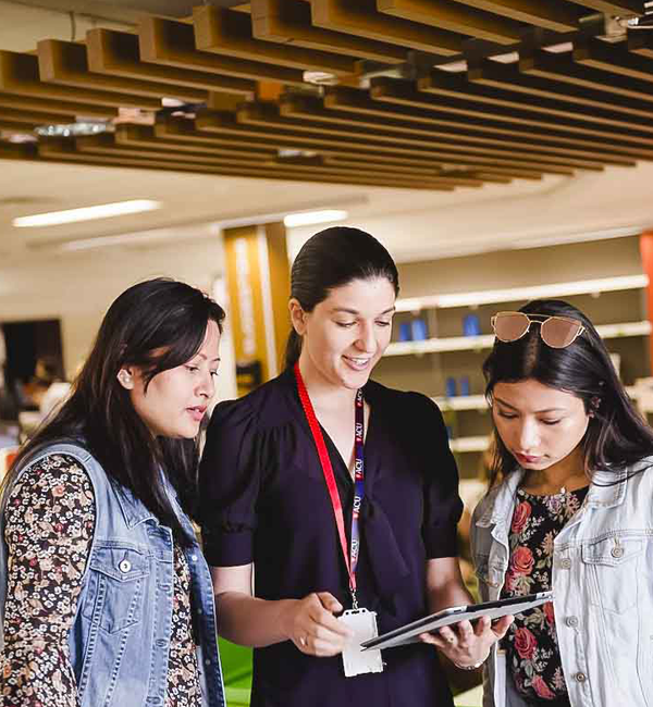 Library staff member assisting two people using a tablet in the library.