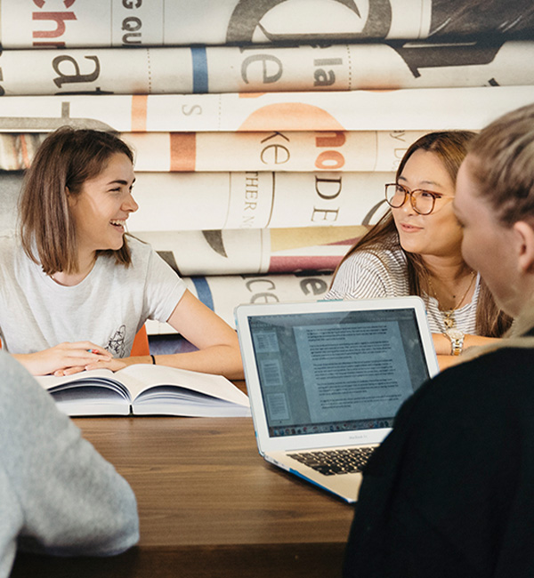 Group of students sitting at a table with an open book and a laptop in the library.